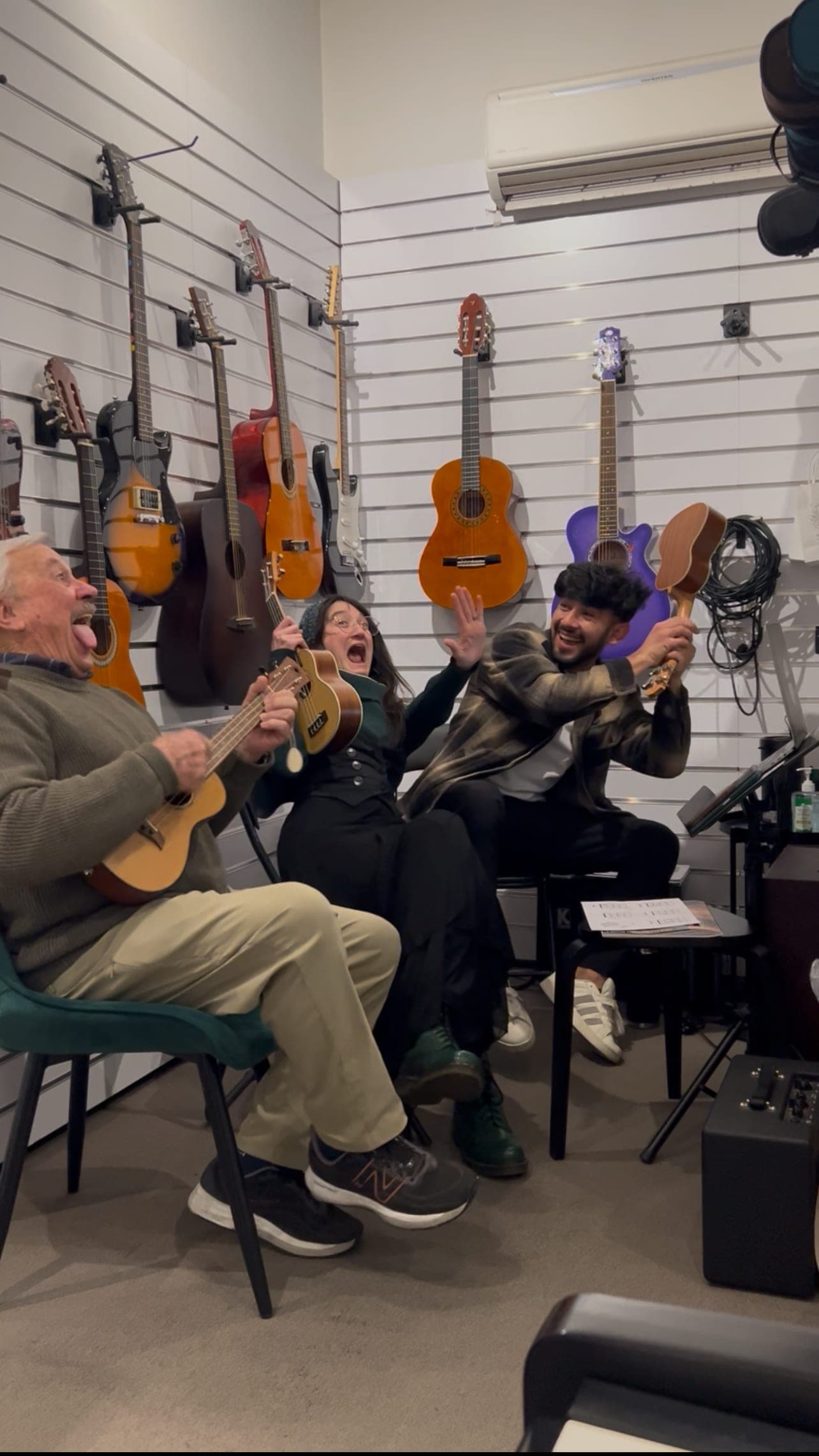 An older man playing a ukulele and laughing while two others cheer him on in the Music Eternal studio